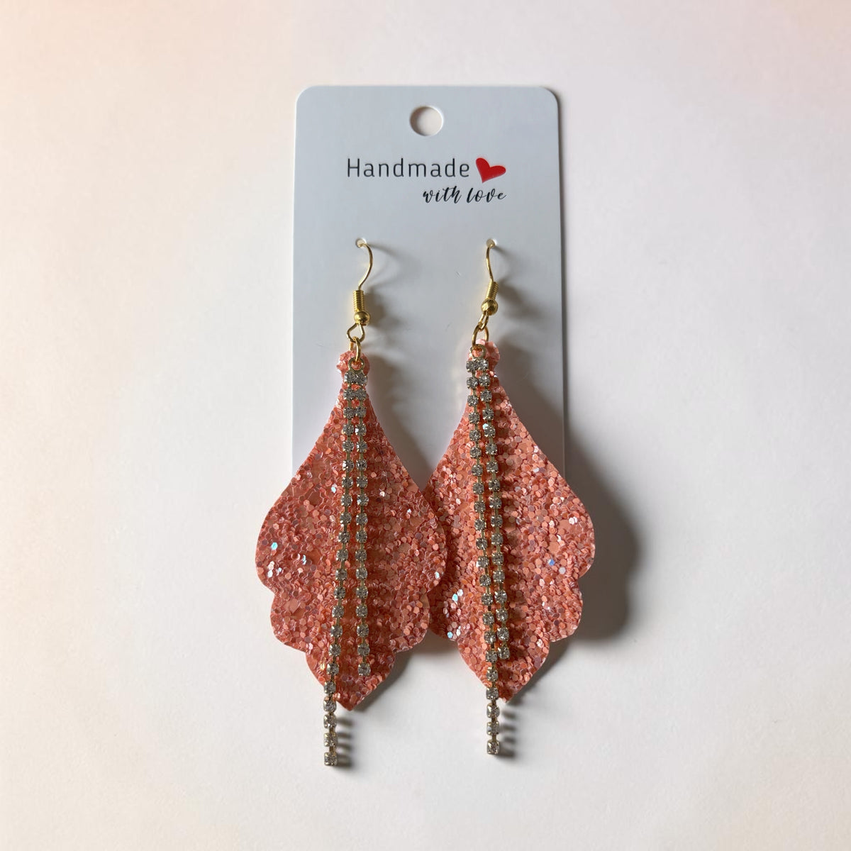 Roselee Glitz coral-pink glitter leaf-shaped dangle earrings with a central rhinestone line and gold-toned hooks.