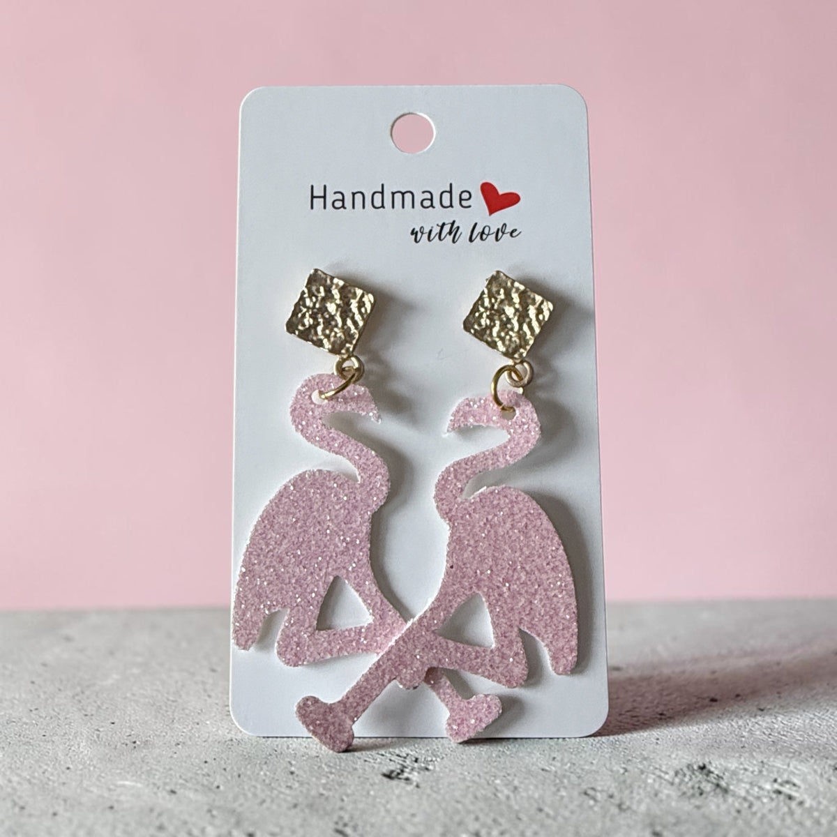 Roselee Glitz pink glitter flamingo dangle earrings with textured gold-tone square studs on a display card